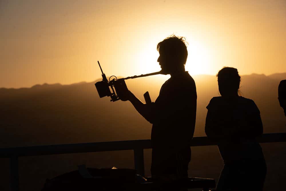Silhouette of a person holding a video camera with the bright yellow sun in the background.