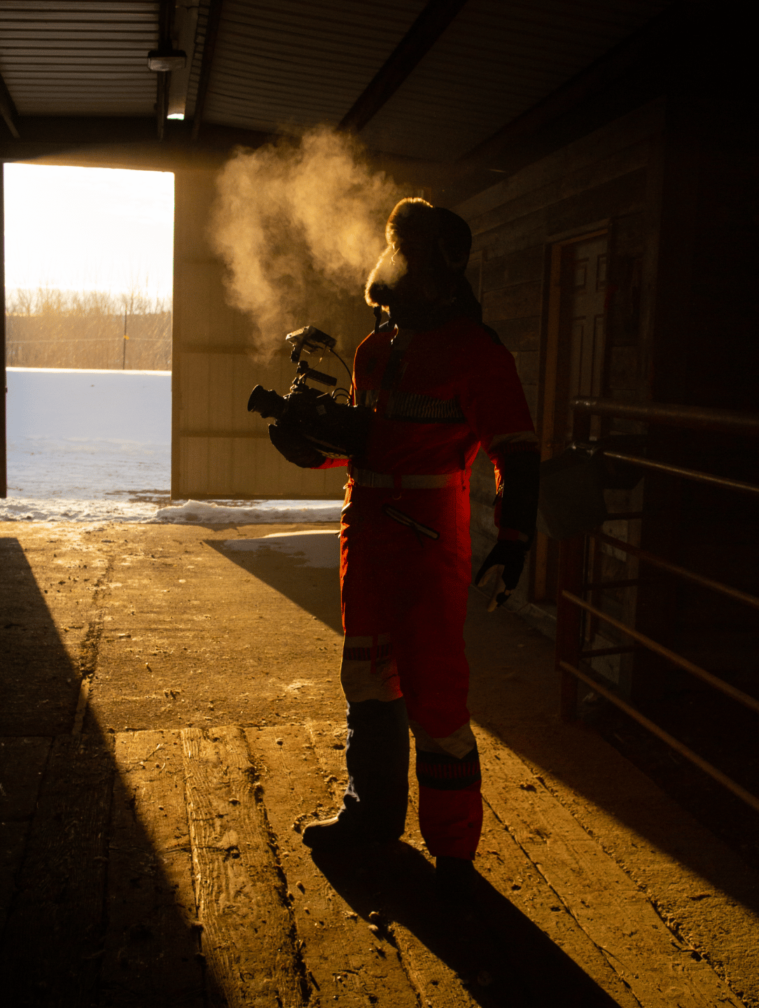 Person in a red outfit holding a video camera in a cold area.