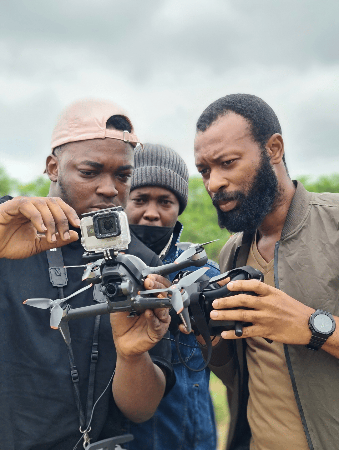 Group of three men holding a drone with a small, portable camera on it.