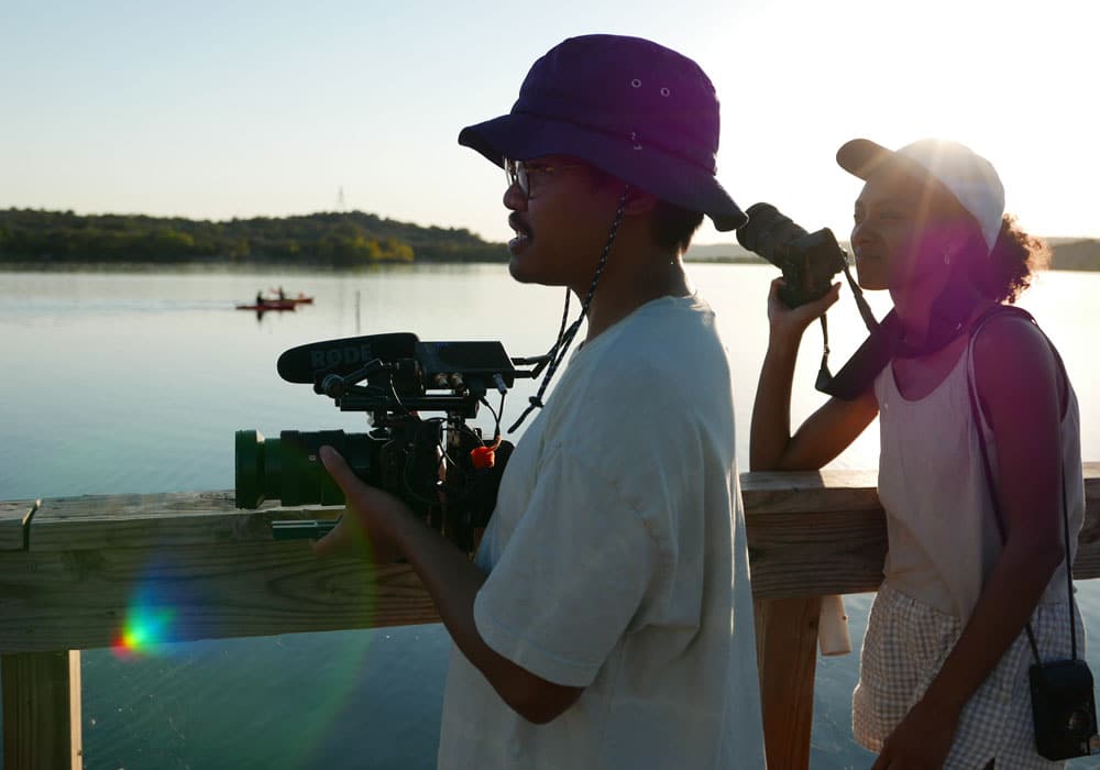 Man and woman holding small video cameras with a lake in the background.