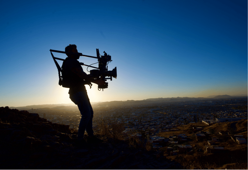 Silhouette of a man holding a large video camera with the sun in the background.